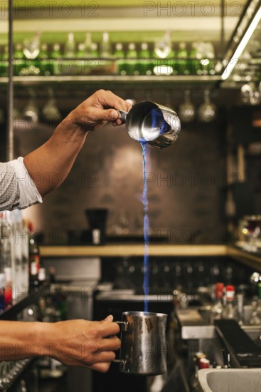 A professional bartender expertly pours a flaming cocktail from a shaker in a stylish bar, showcasing finesse and skill in cocktail preparation and presentation