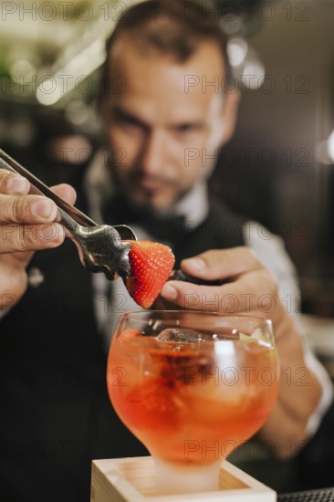 A skilled bartender adds a strawberry garnish to a vibrant cocktail, showcasing his expertise in mixology at a stylish cocktail bar. Focus on precise craftsmanship