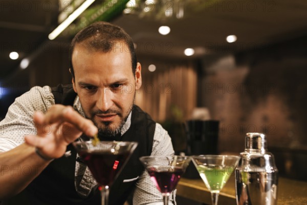 A professional bartender expertly prepares colorful cocktails in a vibrant bar. Focused and skilled, he adds the final touches to his creations in a lively atmosphere
