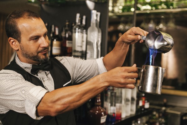 A professional bartender skillfully mixes a colorful cocktail in a chic cocktail bar, demonstrating precision and expertise. Liquor bottles in the background add ambiance
