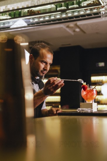 A skilled bartender creates a cocktail, focusing intently on the task. They work in a modern bar setting, surrounded by bottles and glassware, showcasing precision and expertise
