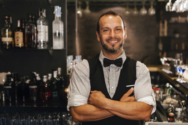 A professional bartender stands confidently in a stylish cocktail bar, surrounded by a selection of spirits. His friendly demeanor and attire add to the sophisticated ambiance