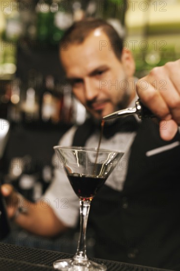 A professional bartender skillfully pours a dark liquid into a martini glass amidst an elegant cocktail bar ambiance. Focus on precision and artistry in bartending
