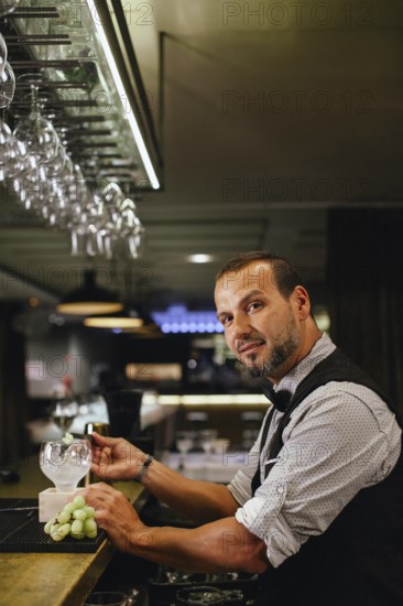 A professional bartender mixes a sophisticated cocktail at an upscale bar. Glasses hang above, and a stylish interior sets the scene for mixological artistry