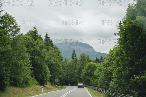 Car traveling on a road surrounded by dense green forests with a view of the foggy mountains in the background, capturing the serene journey through Slovakia's natural landscapes