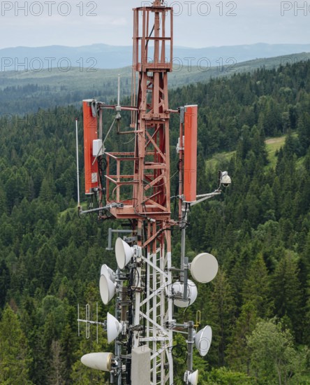 Detailed view of a telecommunication tower equipped with antennas and radio dishes, prominently standing against a lush green forest background