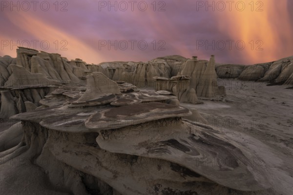 Dramatic sundown illuminates the unique rock formations of Bisti/De-Na-Zin Wilderness in New Mexico, casting surreal colors against the sculpted sandstone