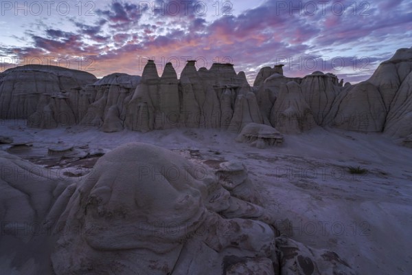 Stunning sunset illuminating the eroded sandstone formations in the Bisti/De-Na-Zin Wilderness, showcasing hues of purple and pink against the New Mexican landscape