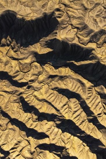 Stunning aerial view of Caineville Mesa in Utah captures intricate desert textures and patterns with deep shadows highlighting the rugged terrain, creating an abstract visual