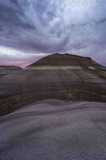 The photo captures dramatic skies at dusk above the layered bentonite hills near Hanksville, Utah, showcasing unique geologic formations and a serene, colorful landscape