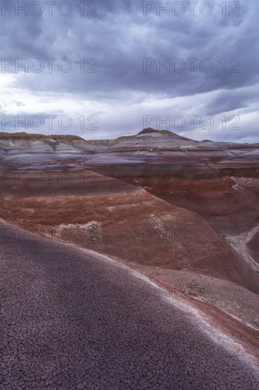 The vibrant, layered Hanksville Bentonites in Utah's desert landscape stretch under dramatic, cloudy skies. The rich colors and textures create an awe-inspiring natural scene