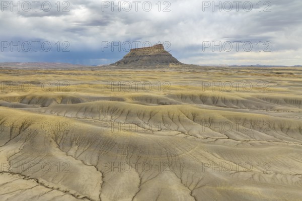 Vast desert landscape with a solitary rock formation under a dramatic sky in Hanskville, Utah. The terrain showcases natural patterns, displaying an array of textures and earthy colors of USA