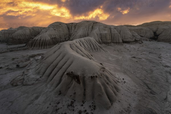 A dramatic sunset illuminates the layered rock formations at Bisti/De-Na-Zin Wilderness in New Mexico, casting a warm glow over the unique landscape