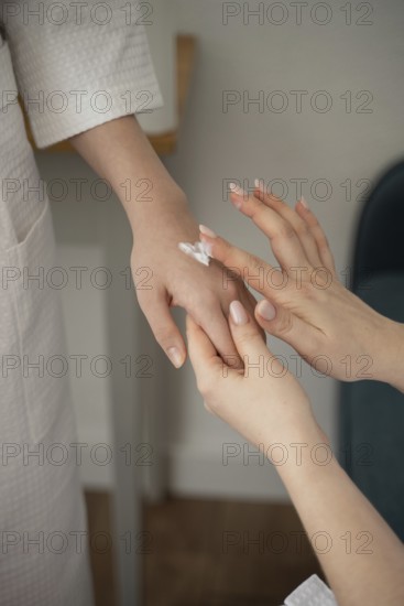 A mother and daughter enjoy a self-care day at home, gently applying lotion to each other's hands. They wear cozy robes, highlighting their nurturing bond and relaxation