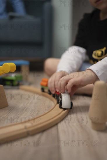 A child sits on the floor, immersed in playing with a wooden train set. The soft focus emphasizes the train, capturing a moment of imaginative play in a cozy home setting