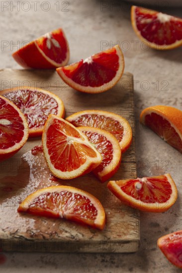 Slices of vibrant blood oranges arranged on a weathered wooden board. The rich red hues and textured surface create an inviting display of natural citrus beauty