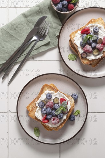 Top view of delicious breakfast setup featuring toast slathered with cream cheese and topped with assorted fresh berries like blueberries, and raspberries, garnished with mint leaves on a ceramic plate