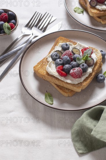 Delicious serving of toast topped with cream cheese and a generous selection of fresh berries including blueberries and raspberries garnished with mint leaves on a stylish ceramic plate