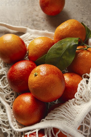 A bunch of vibrant blood oranges with deep red hues sit in a reusable cotton bag on a rustic table. The fresh fruit exudes vivid colors and natural texture
