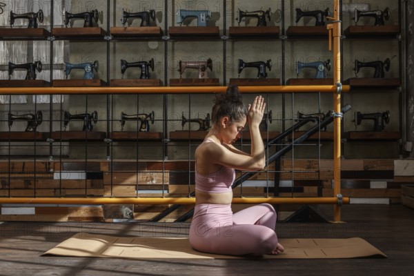 Woman in yoga pose on a mat with sewing machines. Sunlight and vintage machines create a calm, nostalgic atmosphere enhancing the yoga practice's serenity