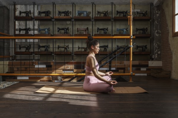In a sunlit room filled with vintage sewing machines, a woman meditates on a yoga mat, practicing mindfulness and relaxation in serene harmony