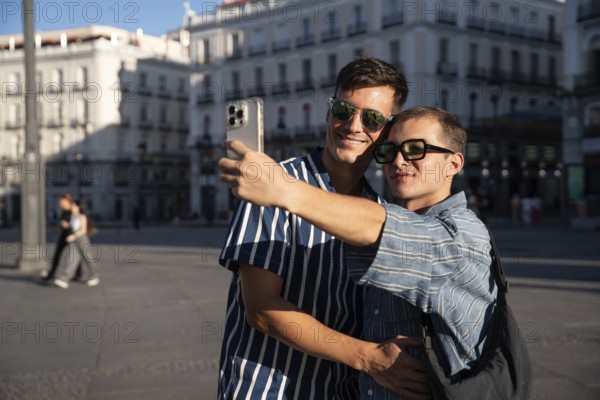 A gay couple joyfully captures a selfie on the vibrant streets of Madrid. The warm sunlight enhances their happiness, celebrating love and pride in this lively urban setting