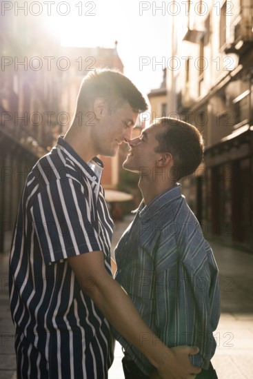 A gay couple embraces tenderly in the sunlit streets of Madrid, celebrating love and diversity. The warm light captures their joyful connection and bright smiles