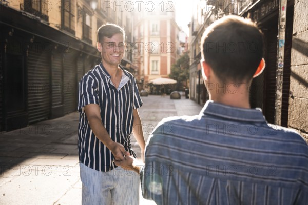A joyful gay couple holds hands while strolling through the charming sunlit streets of Madrid. Their smiles and connection celebrate love and diversity in an urban setting