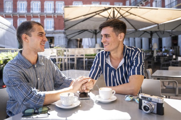 A gay couple shares a tender moment over coffee in the vibrant streets of Madrid. Capturing the essence of love, connection, and diversity in a lively urban setting