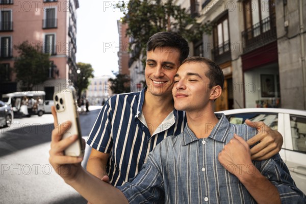 A gay couple happily takes a selfie while exploring the charming streets of Madrid. The vibrant cityscape enhances the joy and celebration of pride and LGBTQIA+ love
