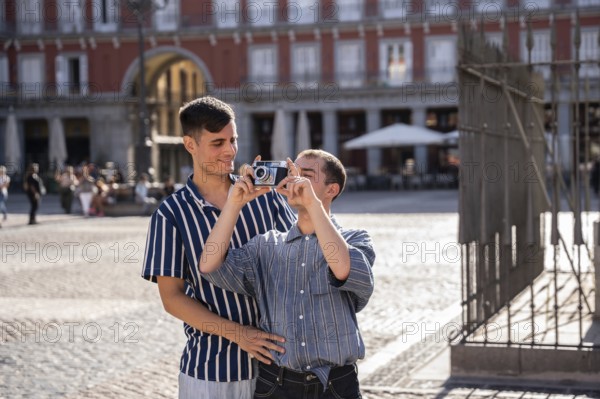 A joyful gay couple enjoys a sunny day in the bustling streets of Madrid. Capturing memories with a camera, they embrace love and happiness in a vibrant urban setting