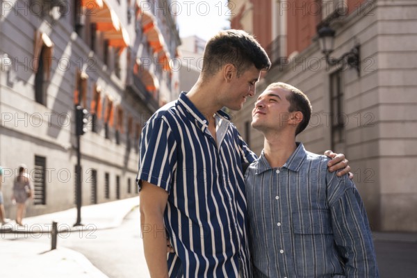 A joyful gay couple embraces while strolling through the picturesque streets of Madrid. Their affection and happiness shine in the sunlit city atmosphere