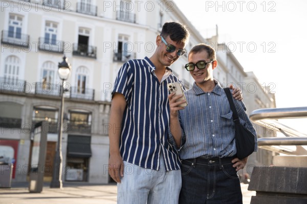 A gay couple enjoys a sunny day, exploring the lively streets of Madrid together. Smiling and looking at a phone, they embody love and connection in an urban setting
