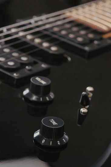 Detailed view of a black electric guitar volume and tone knobs, with strings visible. The image highlights the sleek design and craftsmanship of the instrument, ideal for music themes