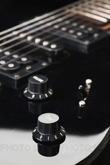 Close up image showcasing the knobs and strings of a black electric guitar, focusing on details that highlight tone and volume controls, illustrating musical craftsmanship