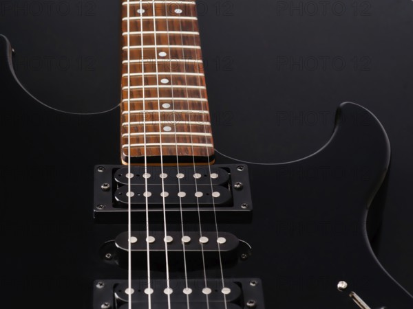 A detailed close up of a sleek black electric guitar with a wooden fretboard and shiny metal strings, set against a dark background. Perfect for music themed projects