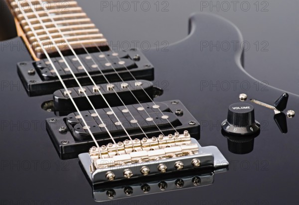 Close up shot of an electric guitar showcasing its strings, pickups, and volume knob. The guitar features a sleek black finish, accentuating its modern design