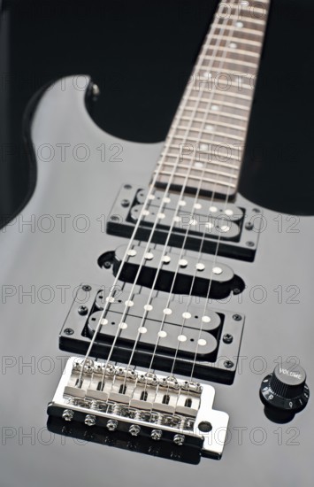 Close up image of a black electric guitar showcasing its strings, pickups, and volume knob. The polished finish and metal elements highlight its intricate design