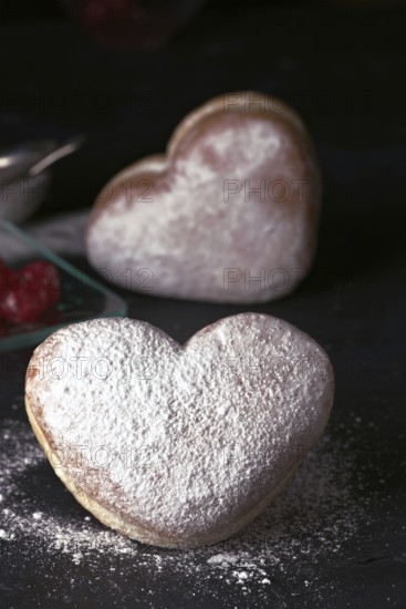 Delicious heart shaped cream buns generously sprinkled with icing sugar, presented on a dark background, ideal for Valentine's Day