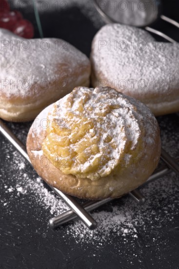 Close up view of scrumptious cream filled buns generously sprinkled with fine icing sugar, presented elegantly on a dark, textured surface