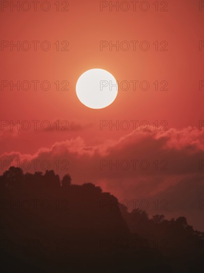An ethereal orange sunset backlights a silhouette of mountainous terrain, expressive of untouched natural beauty and serenity