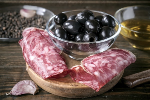 A savory Mediterranean antipasto featuring sliced spanish salami, black olives, garlic, and olive oil. Perfect appetizer arrangement on a rustic wooden table setting