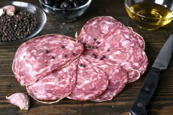 A close up view of spanish salami slices with black peppercorns on a rustic wooden table, alongside garlic cloves and a knife. Ideal for culinary or spanish food themes