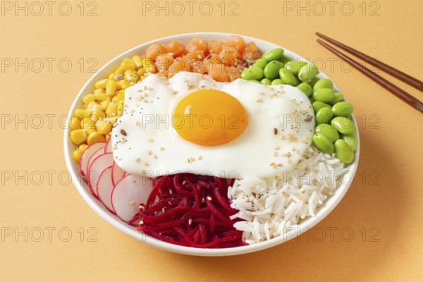 A colorful poke bowl featuring fresh vegetables, rice, and a perfect fried egg on top. Radishes, sweet corn, edamame, and salmon add vibrant colors and flavors