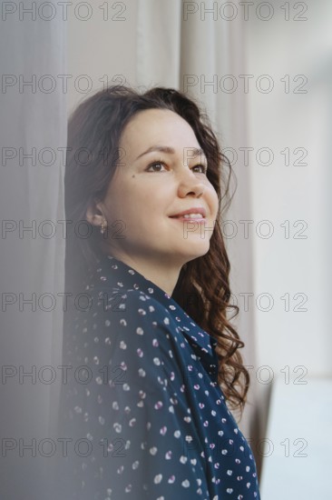 A woman in a patterned blue shirt gazes thoughtfully upward, bathed in soft natural light, creating a serene and introspective mood. Perfect for themes of contemplation and positivity