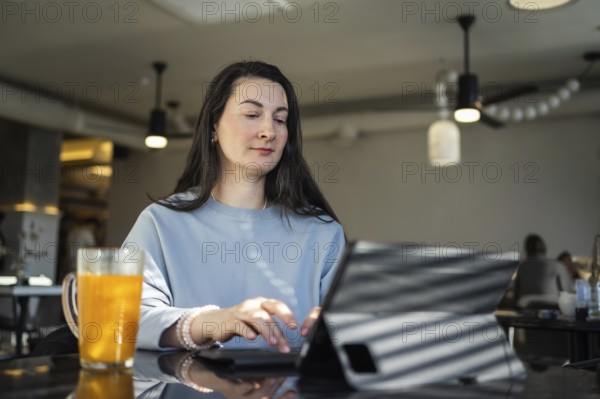 Mid-aged woman browses a tablet at a cafe, staying connected while drinking a glass of orange juice