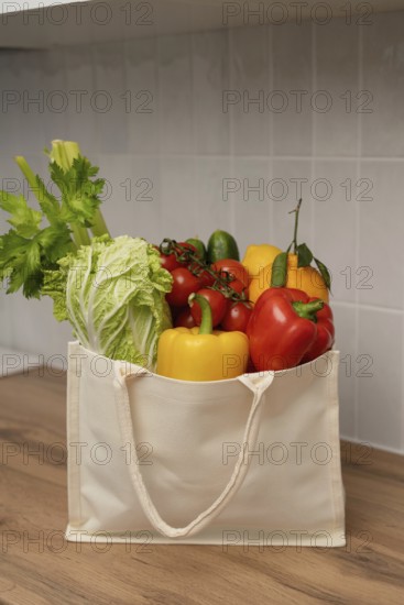 A canvas bag filled with fresh vegetables, including bell peppers, celery, and lettuce, rests on a wooden countertop. A symbol of healthy, sustainable living