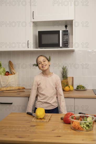 A cheerful child smiles in a modern kitchen surrounded by colorful vegetables, bread, and fresh fruits. A microwave is in the background, adding an urban touch