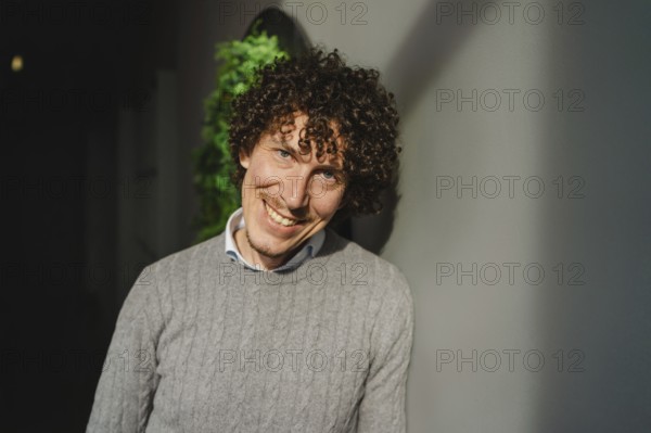 A young man with curly hair stands in front of a green wall, symbolizing themes of ecology and sustainable development. The natural backdrop enhances themes of environmental consciousness