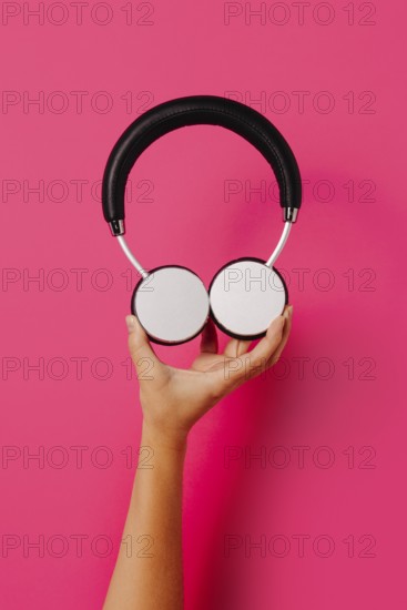 Crop hand holding round shaped lamp with red and white paper hearts on pink background